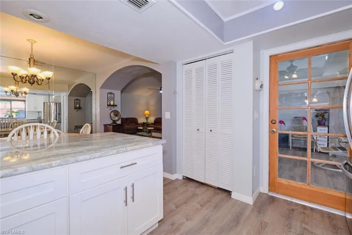 Kitchen with white cabinets, light stone countertops, arched walkways, light wood-style floors, and stainless steel refrigerator with ice dispenser