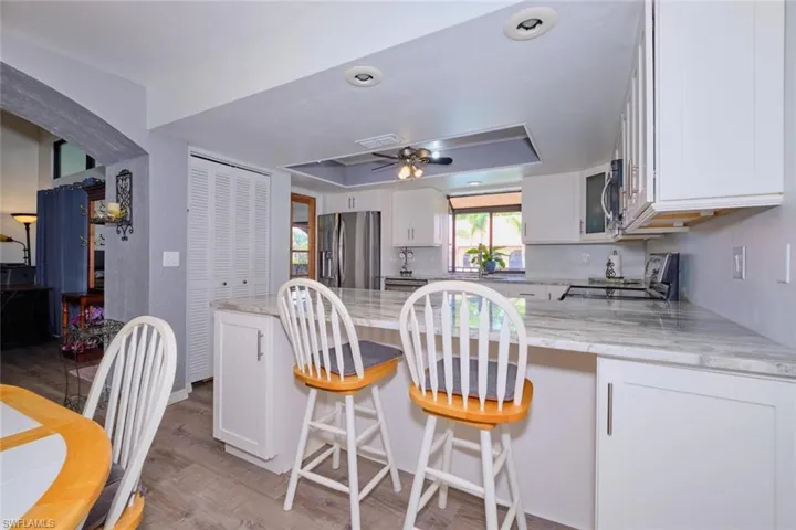 Kitchen featuring white cabinetry, light stone counters, a peninsula, stainless steel appliances, and ceiling fan
