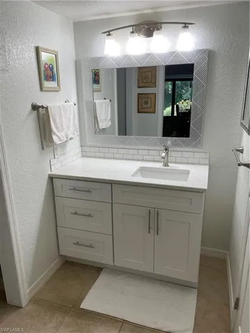 Bathroom featuring a textured wall, vanity, light tile patterned floors, and a textured ceiling