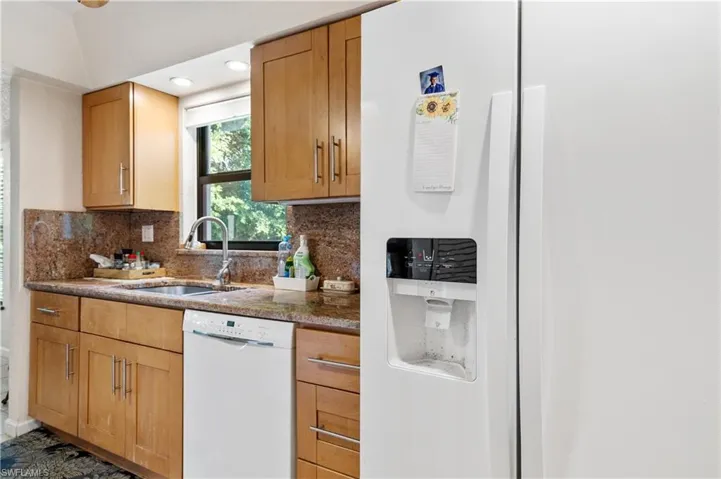 Kitchen with white appliances, a sink, backsplash, lofted ceiling, and dark stone countertops