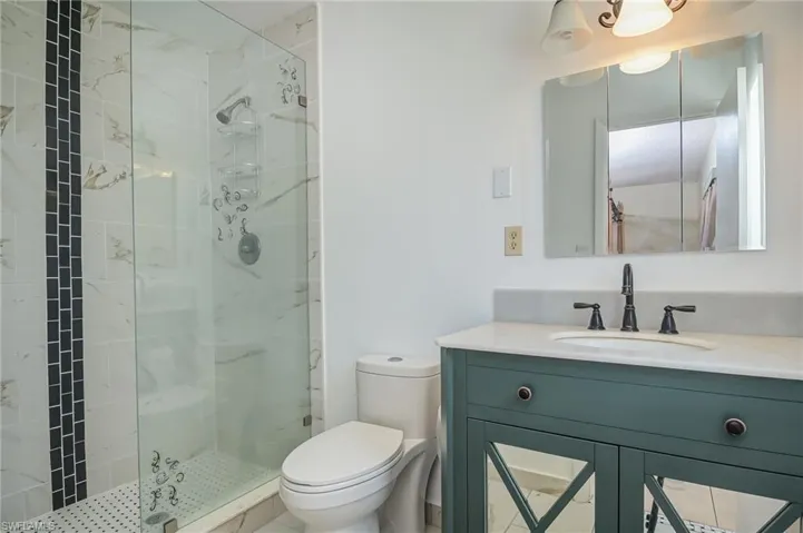 Bathroom featuring a shower with door, vanity, and toilet
