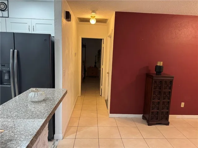 Kitchen with light stone countertops, light tile patterned flooring, stainless steel refrigerator with ice dispenser, a textured ceiling, and white cabinets