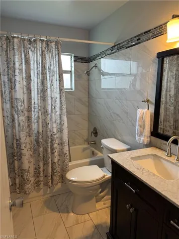 Full bathroom featuring vanity, toilet, tile walls, and shower / bath combo with shower curtain