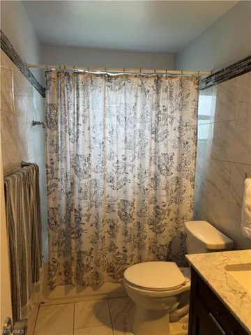 Full bathroom with tile patterned floors, vanity, shower / tub combo with curtain, tile walls, and toilet