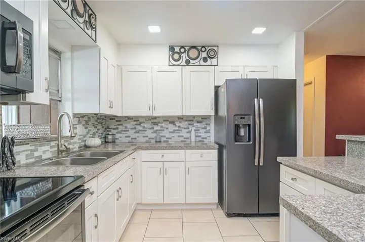 Kitchen featuring sink, white cabinetry, backsplash, appliances with stainless steel finishes, and light stone countertops