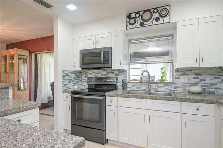 Kitchen with appliances with stainless steel finishes, decorative backsplash, white cabinetry, light stone counters, and sink