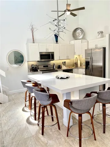 Kitchen featuring a large central island with a solid surface countertop, white cabinetry, stainless steel appliances, and a tiled backsplash