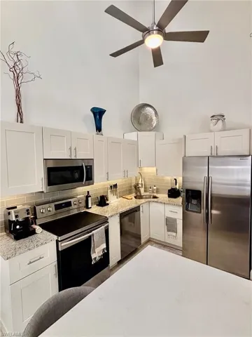 Modern kitchen featuring vaulted ceilings, stainless steel appliances, light cabinetry, granite-style countertops, and a tiled backsplash