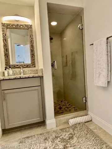 Full glass shower enclosure featuring a mosaic tile floor, alongside a vanity with a stone countertop, an ornate framed mirror, and a wall-mounted light fixture
