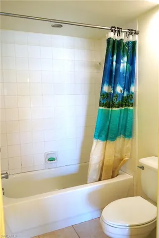 Bathroom featuring tile flooring, shower / bath combination with curtain, and toilet