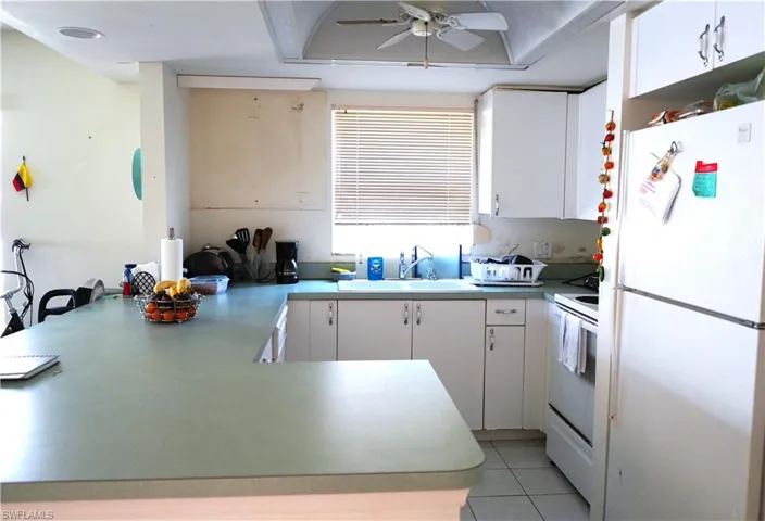 Kitchen featuring ceiling fan, white appliances, light tile flooring, sink, and white cabinetry