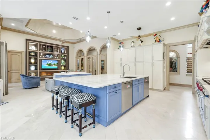 Kitchen featuring a kitchen bar, blue cabinetry, hanging light fixtures, a large island with sink, and crown molding