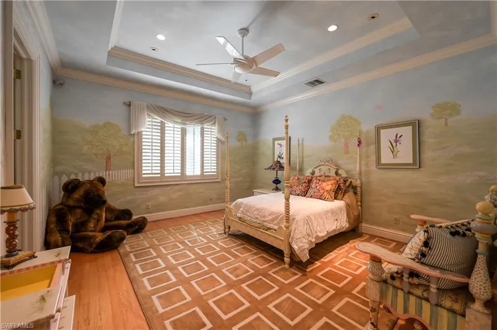 Bedroom with a tray ceiling, ornamental molding, light wood finished floors, and a ceiling fan
