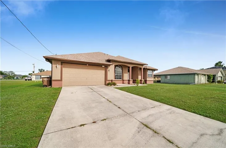 View of front of property featuring a garage, concrete driveway, a front lawn, and stucco siding