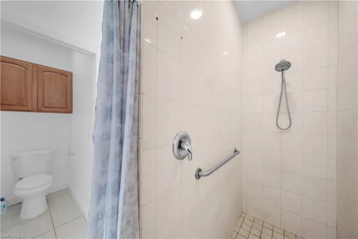Full bath featuring baseboards, tiled shower, toilet, and tile patterned floors