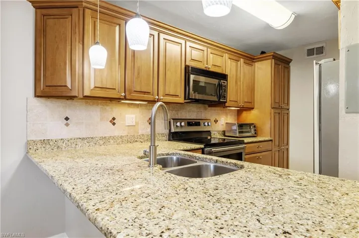 Kitchen featuring light stone countertops, tasteful backsplash, pendant lighting, sink, and appliances with stainless steel finishes