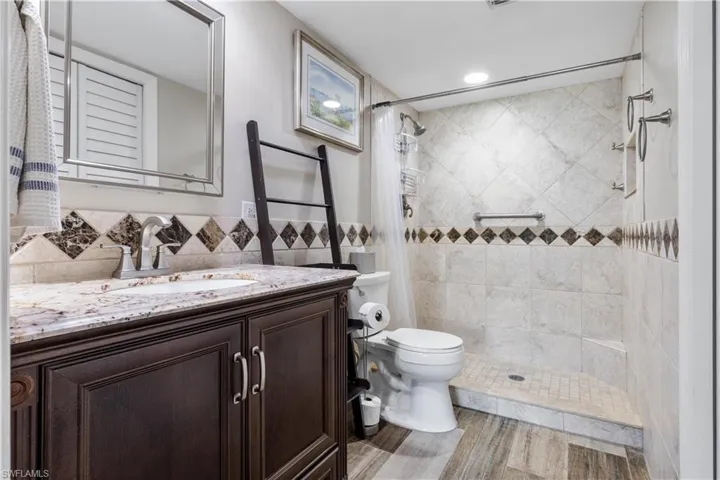 Bathroom featuring tile walls, backsplash, toilet, a tile shower, and vanity