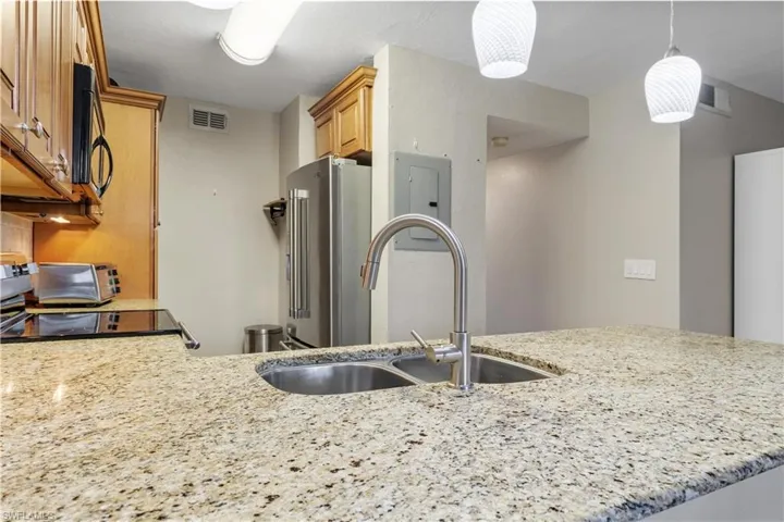 Kitchen with sink, high quality fridge, light stone counters, and hanging light fixtures