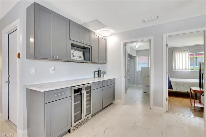 Kitchen with light tile patterned flooring, light stone countertops, wine cooler, and gray cabinetry