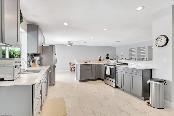 Kitchen with stainless steel electric range, kitchen peninsula, gray cabinets, light tile patterned floors, and ceiling fan