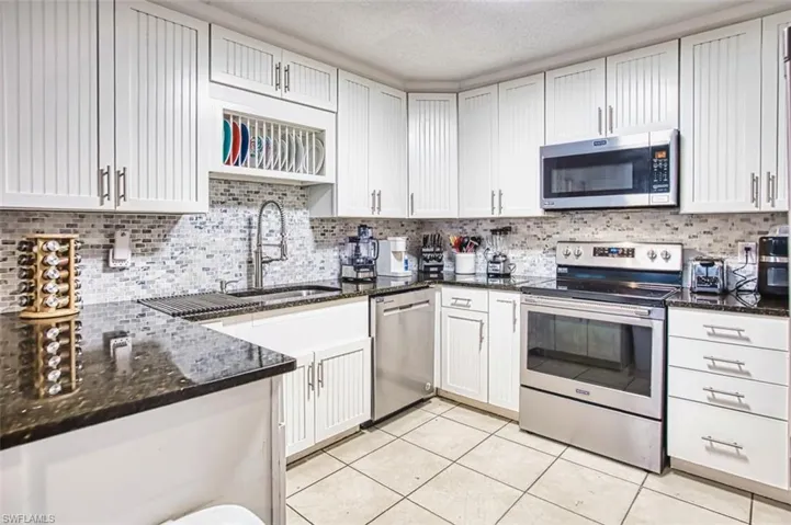 Kitchen with dark stone counters, appliances with stainless steel finishes, a textured ceiling, and white cabinets