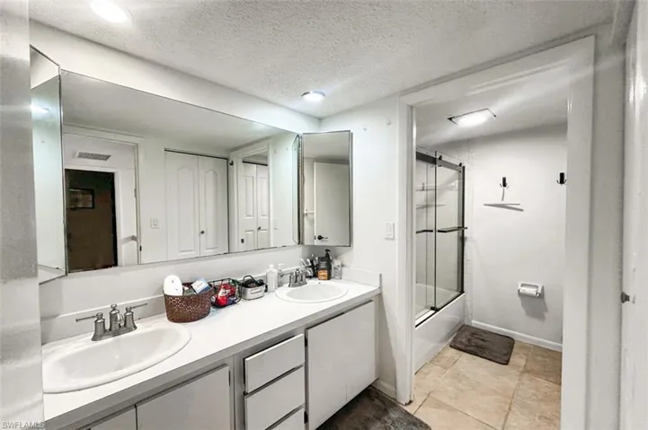 Bathroom featuring combined bath / shower with glass door, a textured ceiling, double vanity, and light tile patterned floors