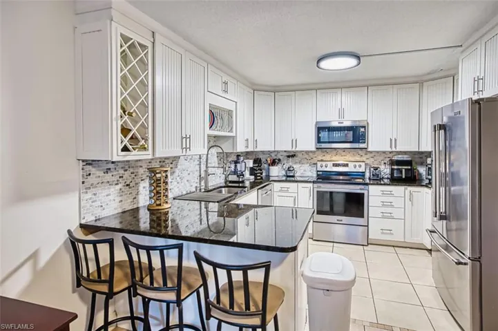 Kitchen with dark stone counters, appliances with stainless steel finishes, white cabinets, a peninsula, and decorative backsplash