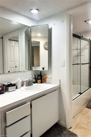 Full bath with vanity, a textured ceiling, combined bath / shower with glass door, and light tile patterned flooring
