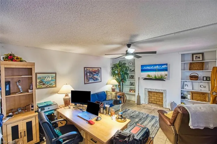 Tiled home office with built in shelves, a ceiling fan, a textured ceiling, and a high end fireplace