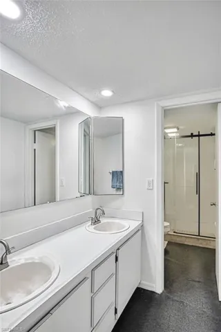 Full bathroom featuring a shower stall, double vanity, a textured ceiling, and recessed lighting