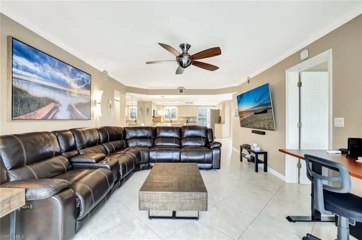 Living room featuring an office area, light tile patterned flooring, crown molding, and ceiling fan