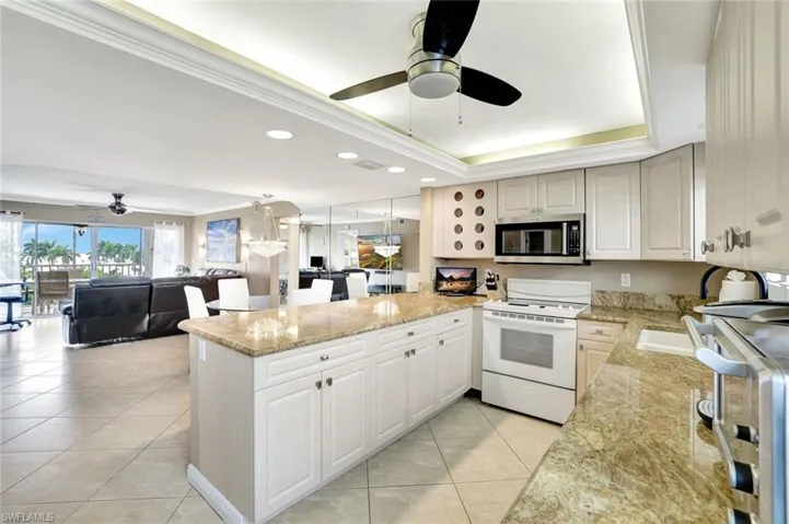 Kitchen with light stone counters, ceiling fan, open floor plan, white range with electric cooktop, and a peninsula