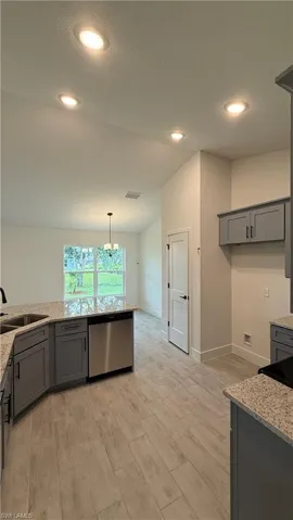 Modern kitchen featuring grey cabinetry, stainless steel dishwasher, speckled countertops, and wood-look tile flooring