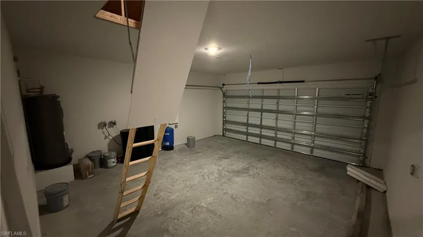Spacious garage featuring a roll-up garage door, concrete flooring, overhead lighting, and an accessible attic opening