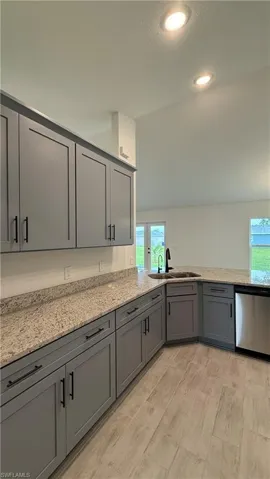 Kitchen featuring gray shaker-style cabinetry, light-toned granite countertops, wood-finish tile flooring, recessed lighting, and a stainless steel dishwasher