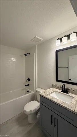 Bathroom featuring a white subway tile tub surround, dark gray vanity with a light granite countertop, and wood-finish flooring