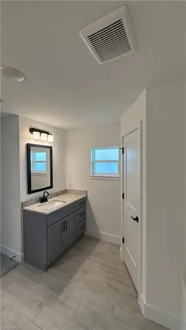 Bathroom featuring a gray vanity with a light-toned countertop, a rectangular sink with a matte black faucet, and a wall-mounted mirror
