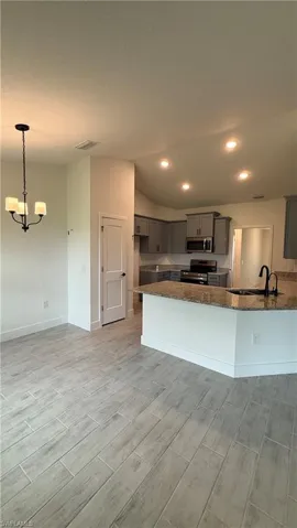 Open-concept living area featuring wood-look tile flooring, a contemporary chandelier, recessed lighting, a kitchen island with stone countertop, and gray cabinetry
