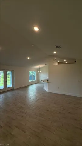 Open-concept living space with wood-finish tile flooring, recessed lighting, vaulted ceiling, and dual-pane glass French doors