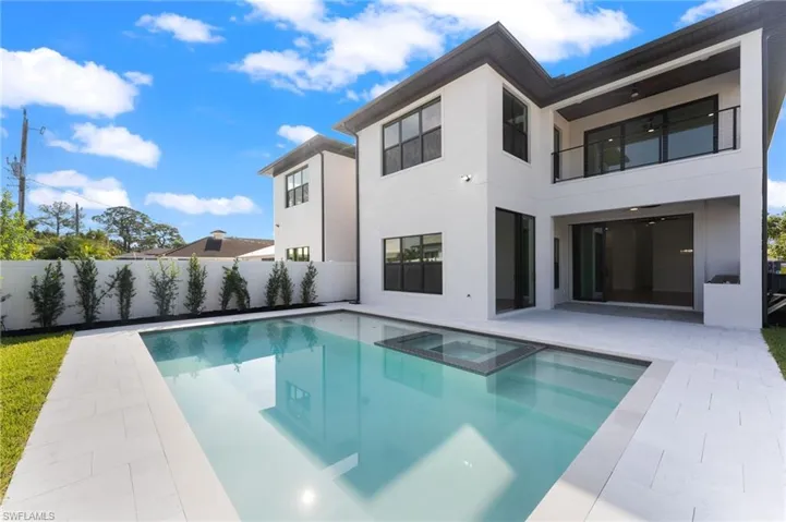 Back of property featuring a swimming pool with hot tub, a patio, and a balcony