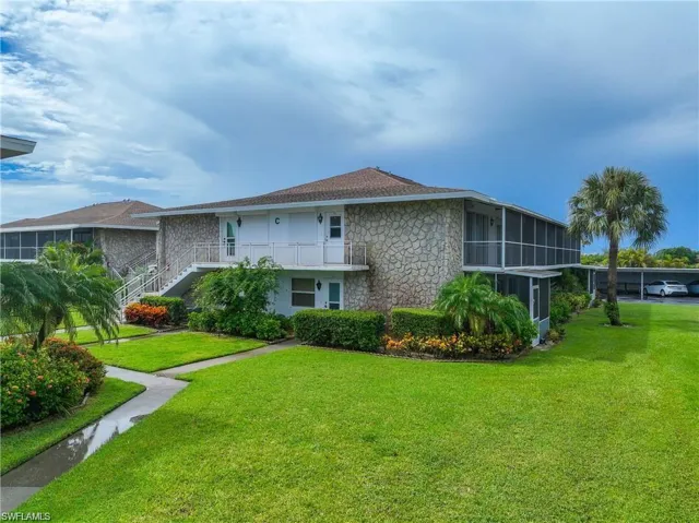 Front exterior of the Naples Florida condo building with mature tropical landscaping and covered parking nearby.