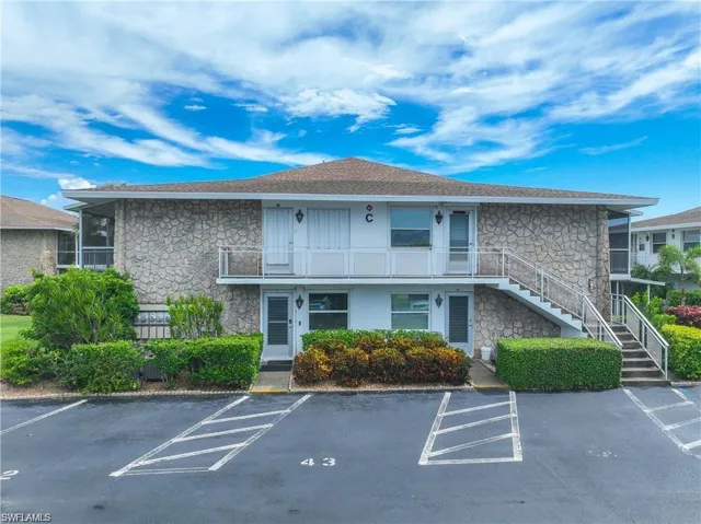 Front exterior of the condominium building with assigned parking and mature tropical landscaping.