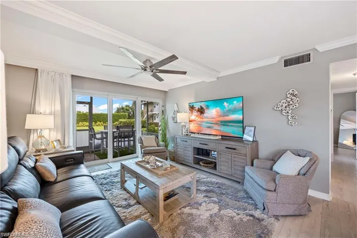 Open living area with tile flooring, ceiling fan, and sliding glass doors leading to the private screened lanai in this Naples Florida condo.