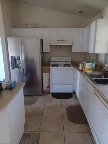 Kitchen with white cabinetry, white appliances, lofted ceiling, light countertops, and exhaust hood