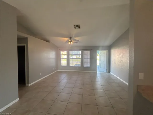 Empty room with a textured wall, light tile patterned floors, ceiling fan, and lofted ceiling