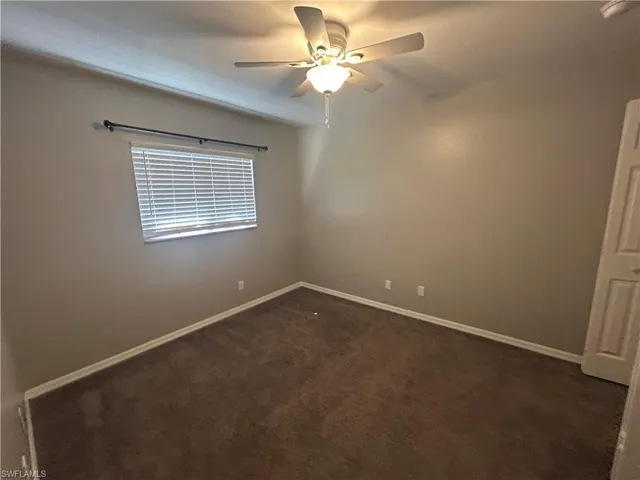 Empty room with dark colored carpet and a ceiling fan
