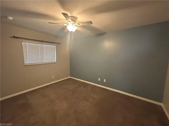 Empty room featuring dark carpet and a ceiling fan