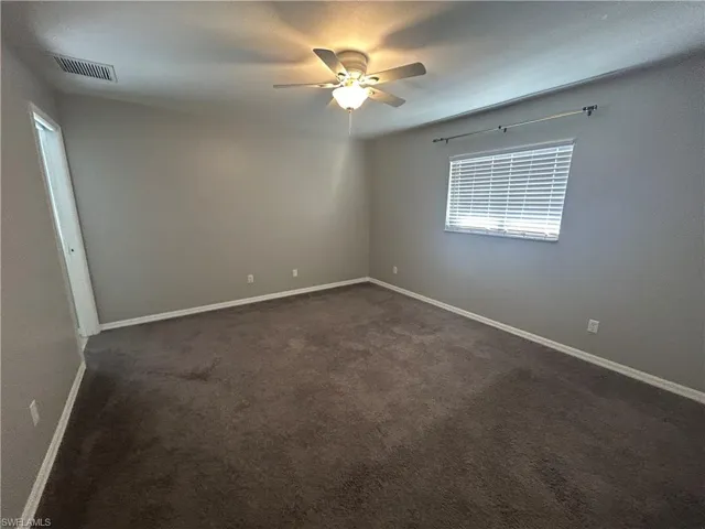 Empty room featuring dark carpet and a ceiling fan
