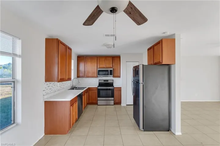 Kitchen with appliances with stainless steel finishes, tasteful backsplash, ceiling fan, sink, and light tile patterned floors