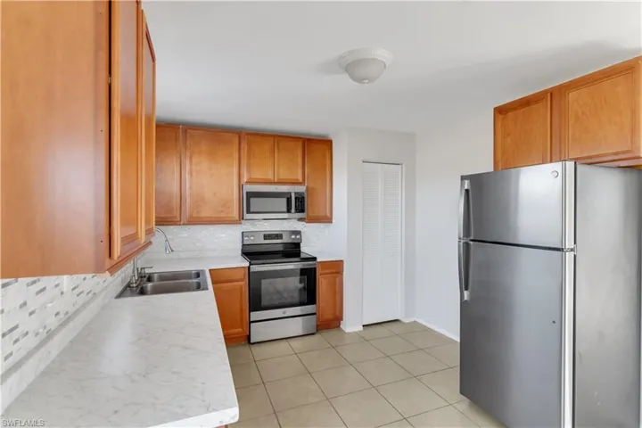 Kitchen with light tile patterned floors, backsplash, stainless steel appliances, and sink
